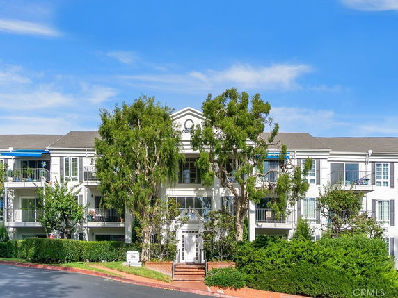 Front view of a three-story building with balconies and trees in front.
