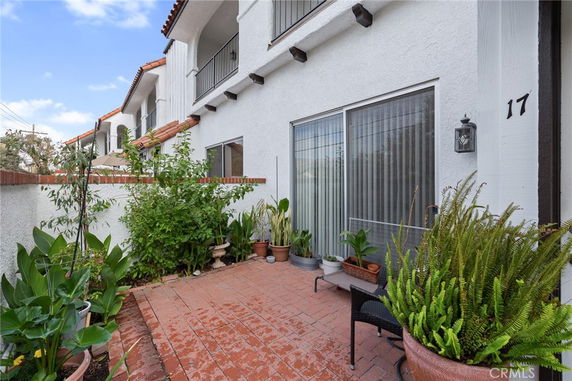 Front view of a white two-story house with a terracotta tiled roof and a small patio area surrounded by plants.