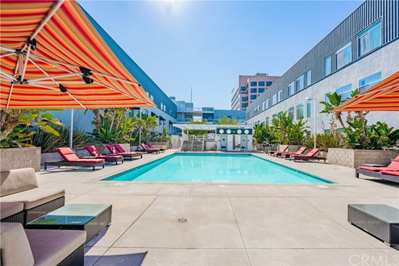 Outdoor swimming pool area with sun loungers and umbrellas in a modern building complex.