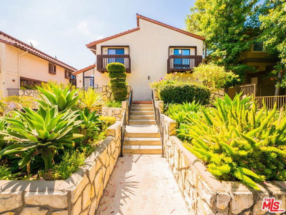 Front view of a two-story house with balconies and a stone-bordered walkway.