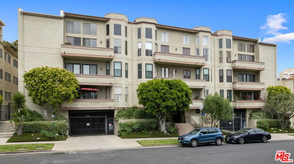Front view of a multi-story apartment building with balconies and ground-level parking.