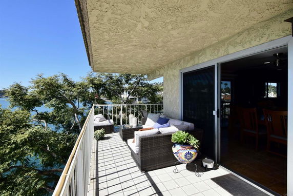 Balcony with outdoor seating overlooking a view of trees and water.