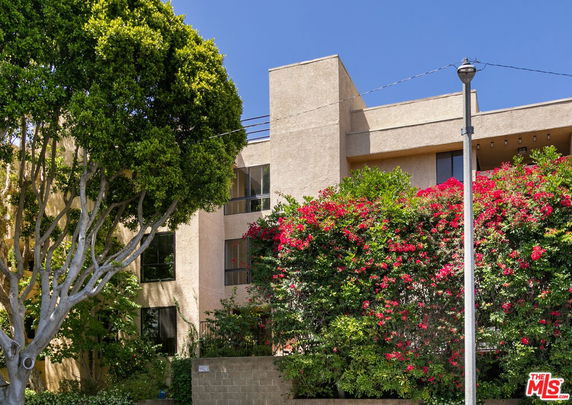 Front view of a multi-story building with beige exterior and lush greenery.