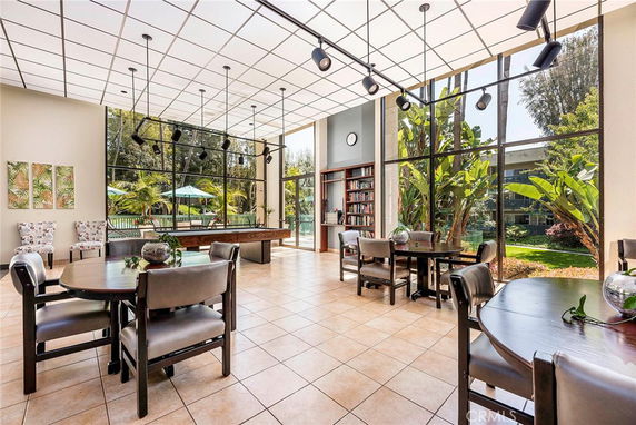 Interior view of a room with tables, chairs, and large windows facing a garden area.