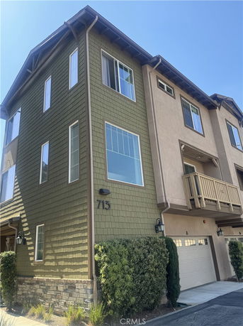 Front view of a multi-story house with green siding and beige stucco, featuring a garage and small balcony.