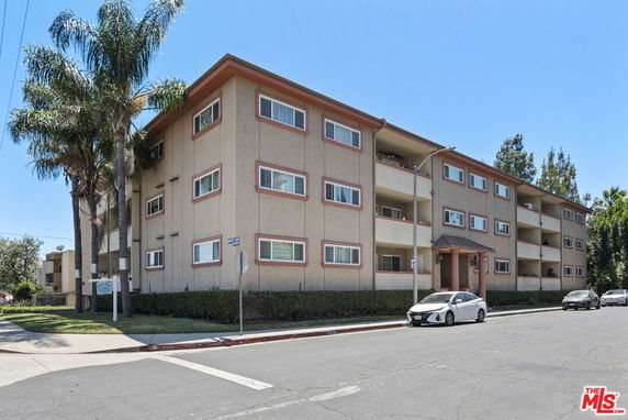 Front view of a multi-story apartment building with balconies and a street in the foreground.