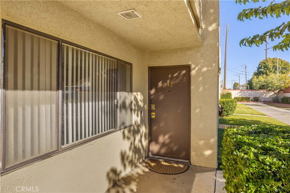 Front view of a building entrance with a brown door and a window with blinds.