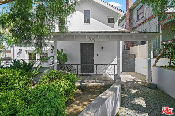 Front view of a two-story house with a small porch and decorative plants.