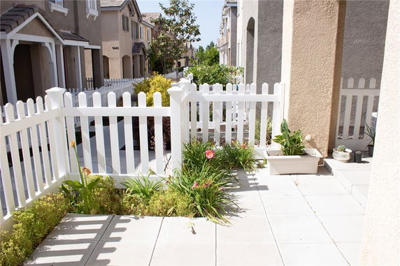 View of a row of townhouses with a white picket fence and small garden in front.