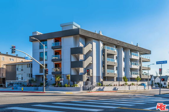 Front view of a modern multi-story building with balconies located at a street intersection.