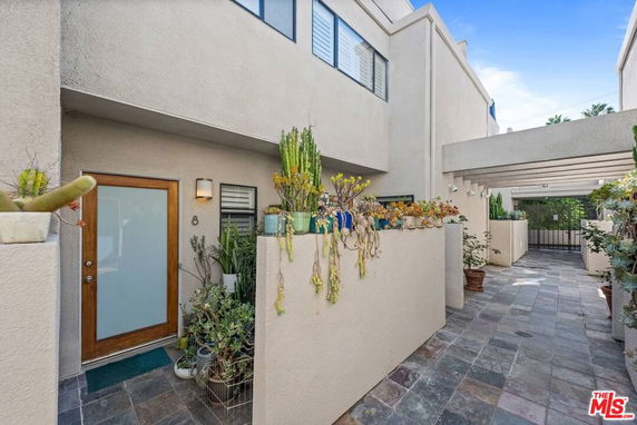 Front view of a modern townhouse entrance with potted plants and a gated walkway.