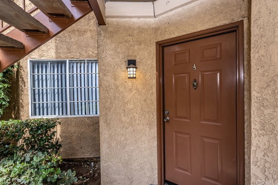 Front view of an apartment entrance with a brown door and adjacent window under a staircase.