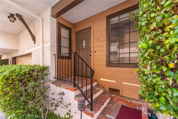 Entryway to a house with steps leading up to the front door, featuring brick accents and a beige exterior.