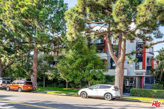 Front view of a multi-story residential building with balconies, partially obscured by trees.