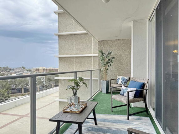 Balcony with chairs and a table, overlooking a distant cityscape.