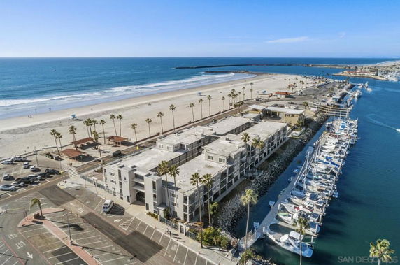 Aerial view of a coastal area with a beach, marina, and adjacent buildings.