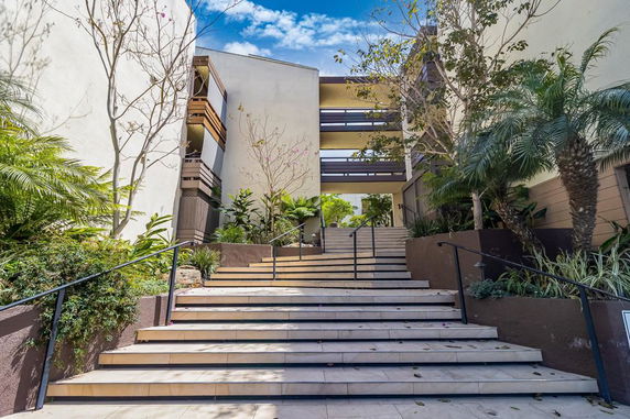 Front view of a multi-story building with stairway entrance and surrounding plants.