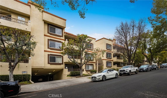 Front view of a multi-story residential building with balconies and a parking area underneath.