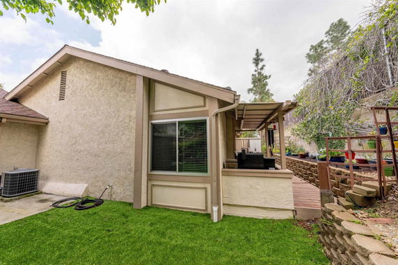 Rear view of a house with covered patio and greenery.