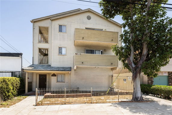 Front view of a three-story residential building with balconies and a gated front yard.