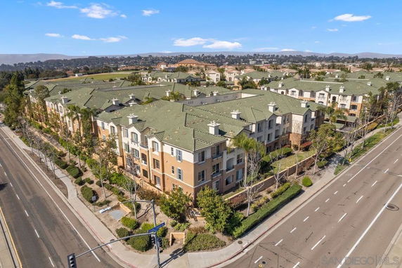 Aerial view of a multi-story apartment complex with green roofs and beige exteriors alongside a road.