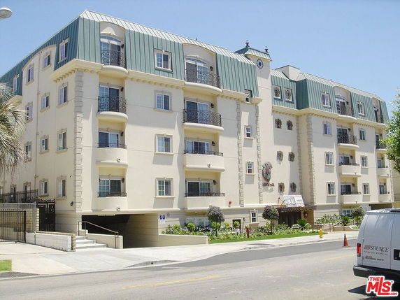 Front view of a multi-story apartment building with a distinctive green roof and balconies.