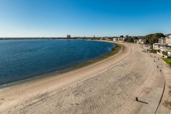 Wide-angle view of a sandy beach and calm water with buildings in the distance.