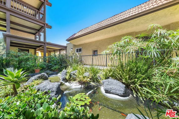 Building exterior with balcony and garden area featuring a pond and plants.