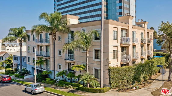 Front view of a multi-story apartment building with balconies and surrounding palm trees.