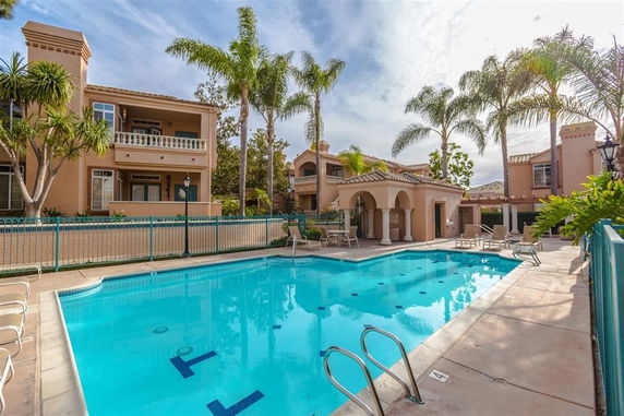 Outdoor swimming pool area with surrounding palm trees and apartment buildings.