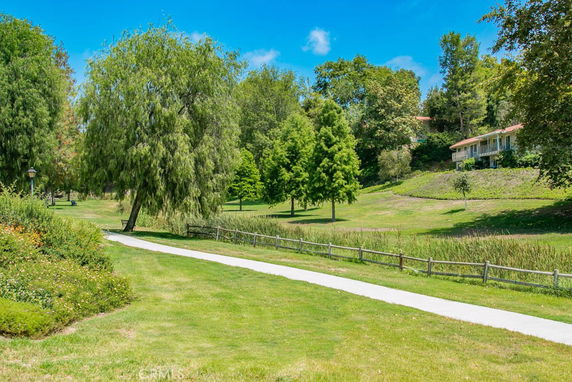 Pathway through a grassy area with trees and a house in the background.