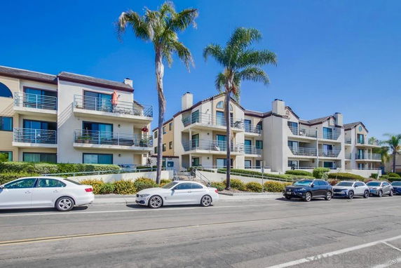 Front view of a multi-story apartment building with balconies and palm trees.