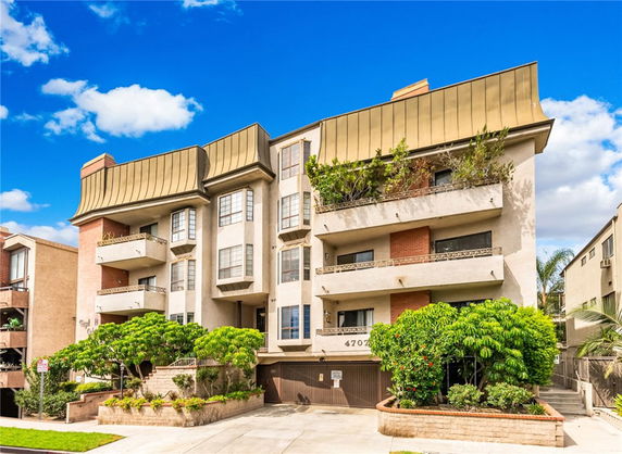 Front view of a multi-story building with balconies and a distinctive sloped roof.