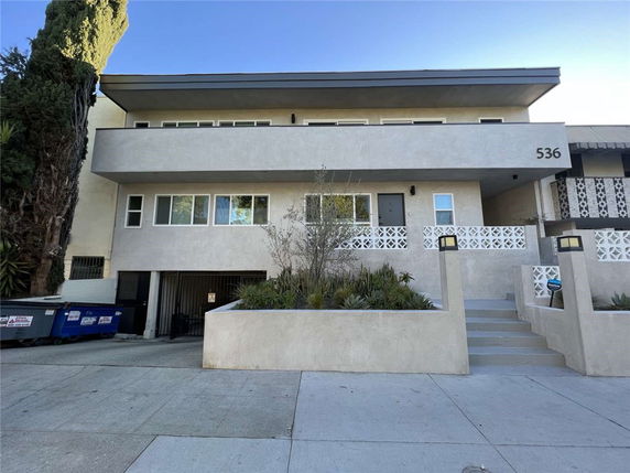 Front view of a multi-story residential building with a flat roof and gated entryway.