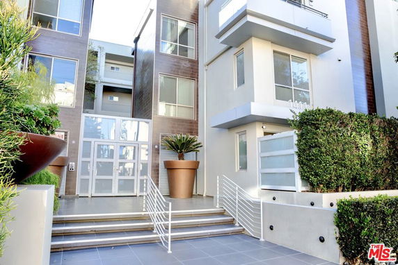 Front view of a modern multi-story apartment building with large windows and a staircase leading to the entrance.