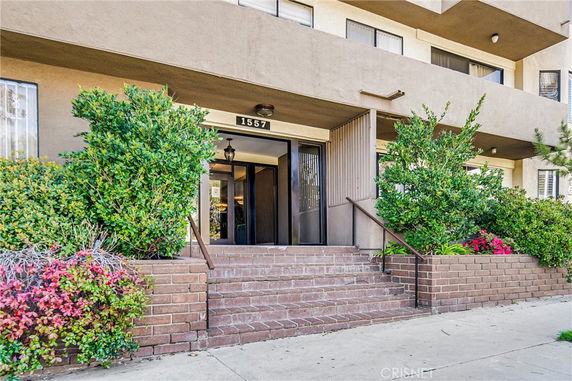 Front view of a multi-story building entrance with brick steps and greenery.