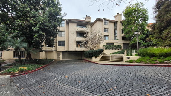 Front view of a multi-story residential building with multiple balconies and surrounded by trees.