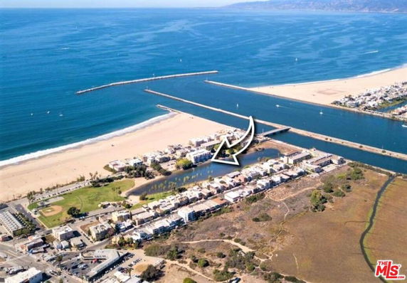 Aerial view showing a coastal area with a beach, canal, and residential buildings.