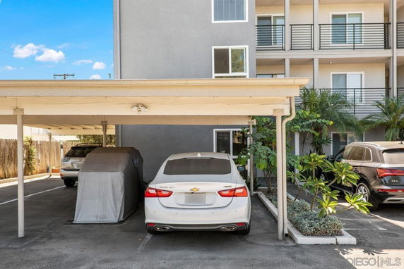 Outdoor parking area with covered parking structure and multiple vehicles.
