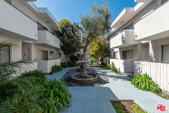 Front view of a multi-story residential building with balconies and a central walkway featuring a fountain.
