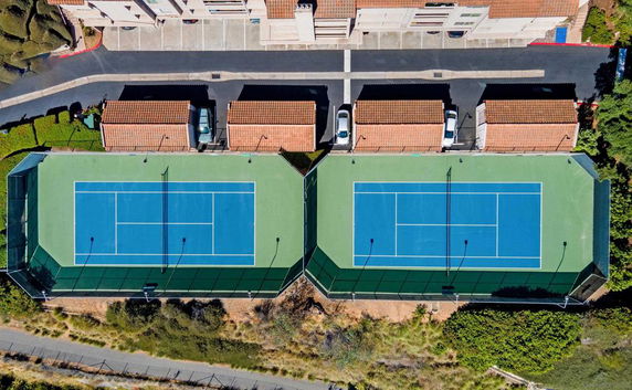 Aerial view of two adjacent tennis courts with surrounding fences and nearby parking area.