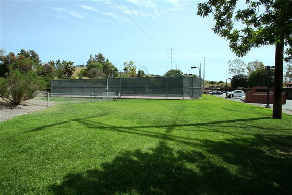 View of an outdoor tennis court surrounded by a grassy area and fence.