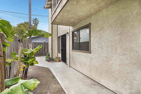 Exterior view of a building with stucco walls and a small garden area beside a pathway.