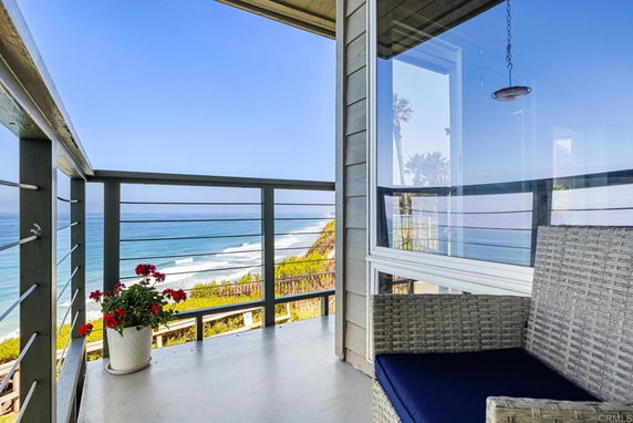 Balcony view overlooking the ocean with railing and a chair.