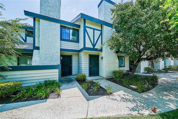 Front view of a multi-story townhouse with blue accents and surrounding greenery.