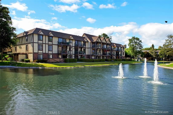 Front view of a multi-story building with Tudor-style architecture next to a pond with fountains.