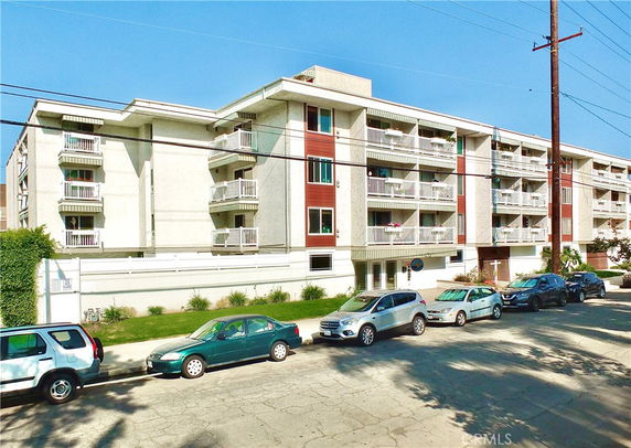 Front view of a multi-story apartment building with balconies and street parking.