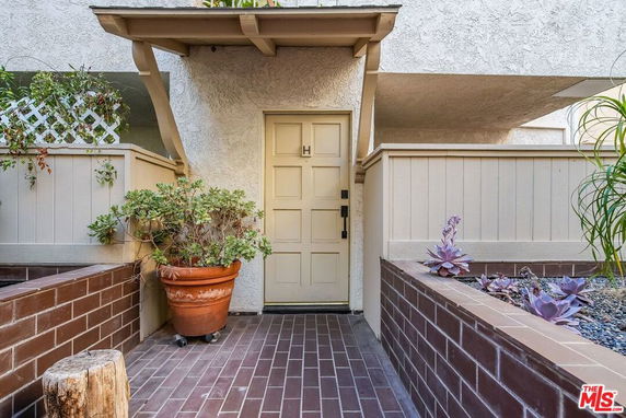 Front view of a house entrance with a beige door and plants.