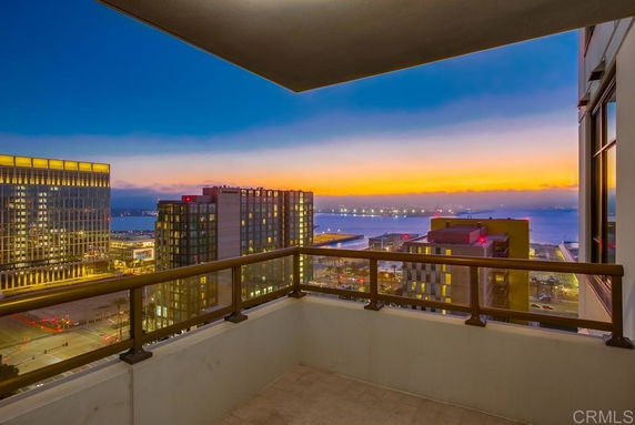 Panoramic view from a high-rise building balcony overlooking city skyline and waterfront at sunset.