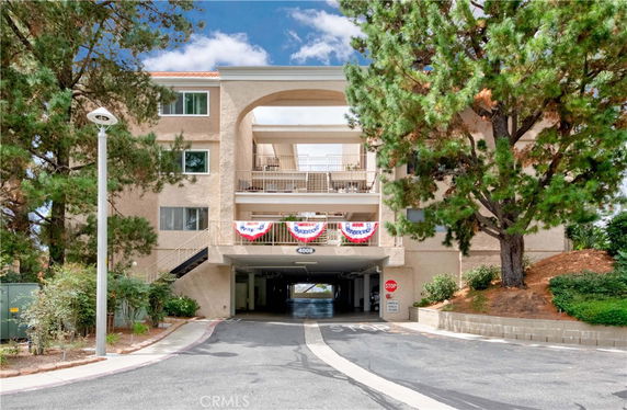 Front view of a multi-story building with open balconies and a parking area underneath.